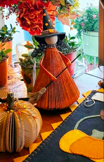 A decorative witch made from a carved and painted book, with a pointy hat, broom, and hair made from pipe cleaners
