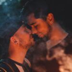 two lightly tanned-skin men nuzzle each other by sparklers