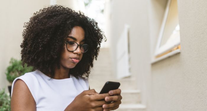 a Black woman with thick curly hair looks at her phone