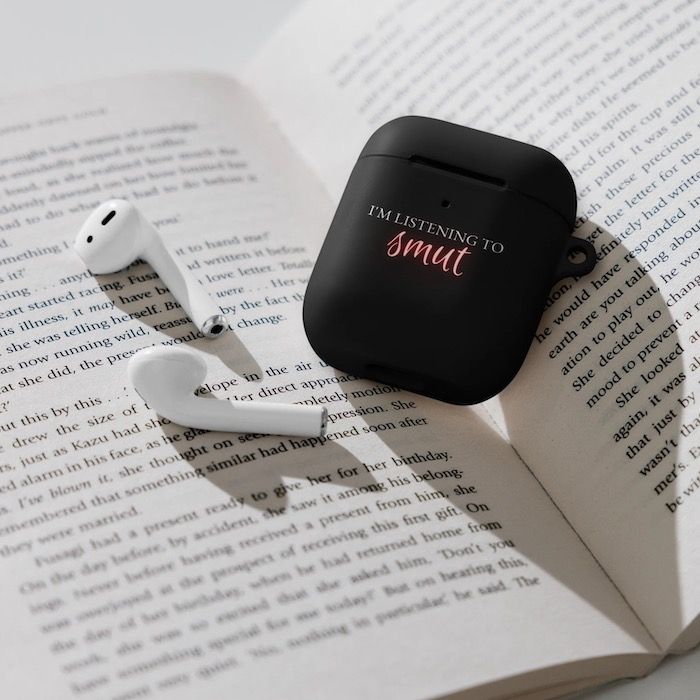 a pair of AirPods next to a black AirPods case with the words "I'm listening to smut"  in pink text