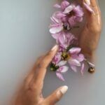 brown hands in cloudy water with floting purple flower petals