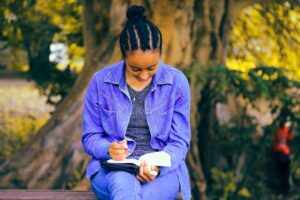 Back woman sits writing in a notebook