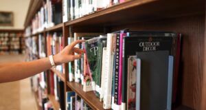 lightly complected hand reaching for a book in a library