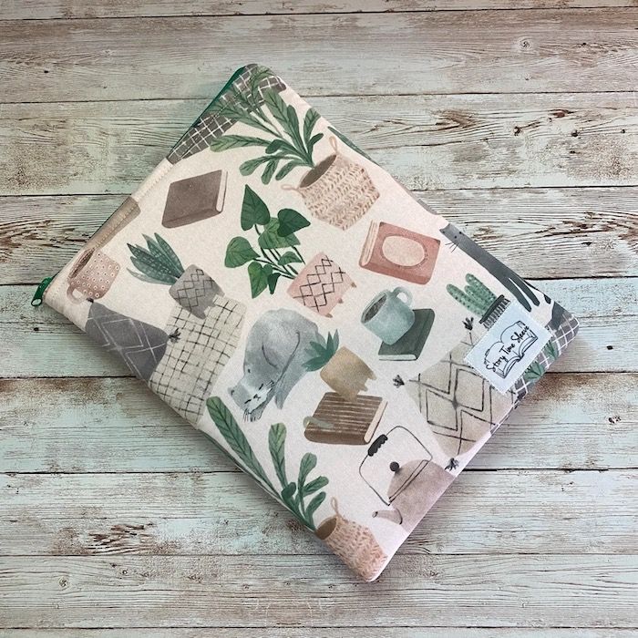 cream book sleeve with a pattern of plants, books, coffee mugs, and cats, all in soft colors
