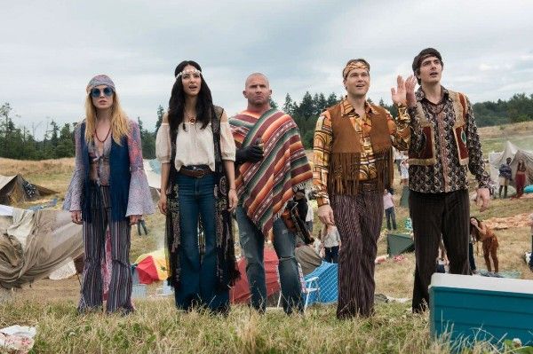 A still from Legends of Tomorrow, showing White Canary, Zari (Tala Ashe), Heatwave, Steel, and the Atom all dressed as hippies at Woodstock and looking bemused.
