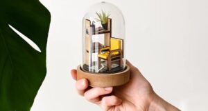 a photo of a hand holding up a library craft kit under a glass cloche