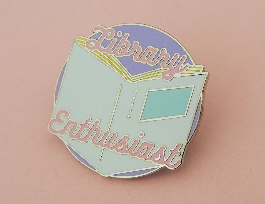 Image of a round pin on a pink background. It says "library enthusiast" in pink and has a pastel color book. 