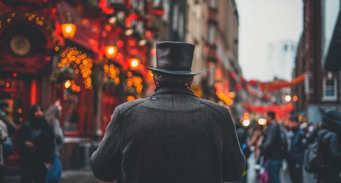 man in topcoat with back to camera stands on a magical looking London street