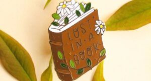 a photo of a book enamel pin with flowers that says Lost In a Good Book