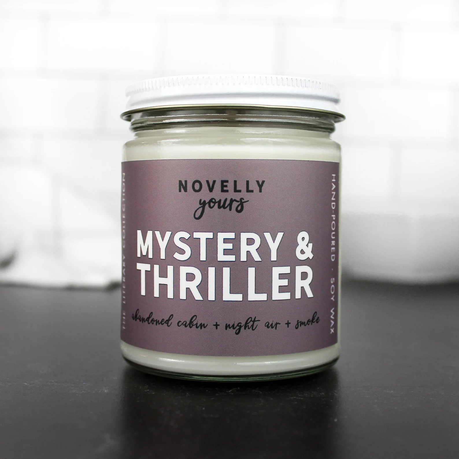 Glass jar candle with a purple label that reads "Mystery and Thriller"
