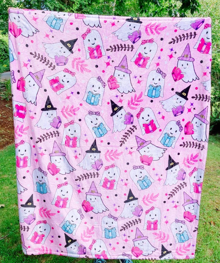 Image of a pink blanket. The blanket has white ghosts in hats and bows reading books. 