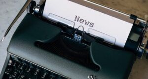 a black typewriter with a sheet of white paper bearing the word "News"
