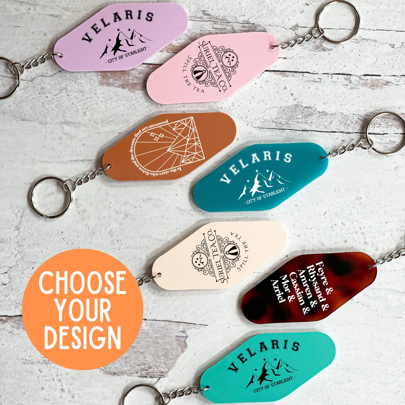 A photo of 7 hotel keychains. Top to bottom, the keychains are lavender with the words Velaris City of Starlight written on it, pink with the words Suriel Tea Co Spill the tea written on it, orange with the words to the stars who listen and the dreams that are answered written on it, blue with the words Velaris City of Starlight written on it, cream Suriel Tea Co Spill the tea written on it, red with character names written on it, and teal with the words Velaris City of Starlight written on it.