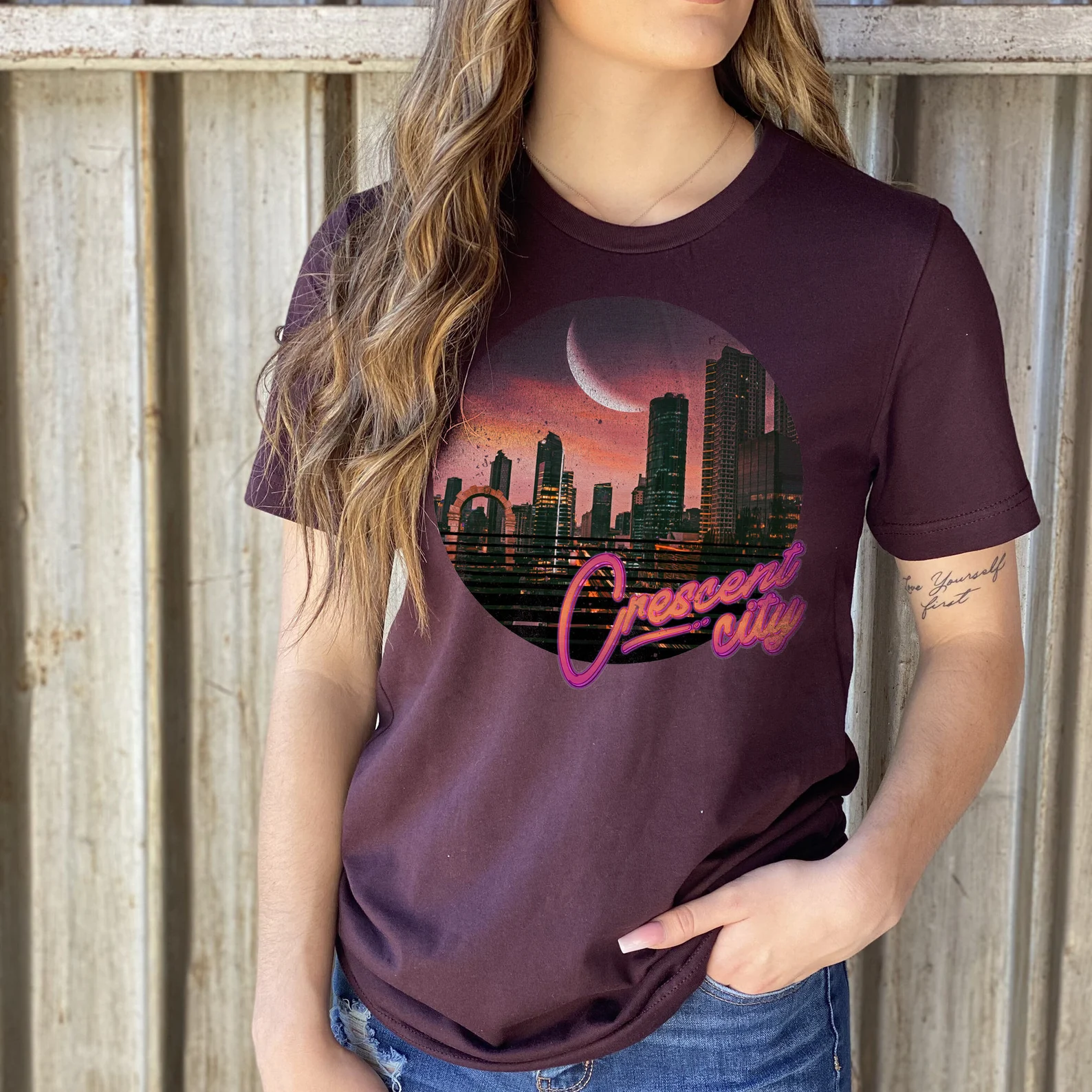 A photo of a person with long brown hair wearing a purple shirt with a night skyline of a city and crescent city written on the front. 