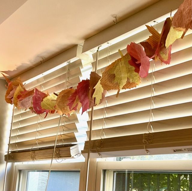 A colorful garland of watercolor painted leaves made from old books strung across the top of windows with white blinds