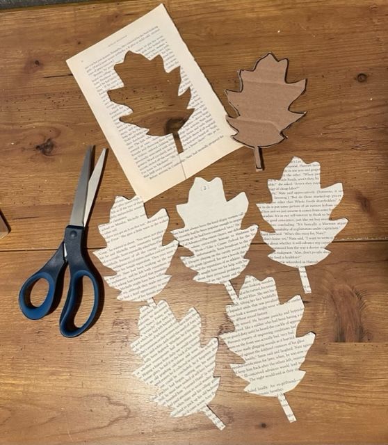 Five leaf shapes have been cut from old book pages and are displayed next to the stencil and a pair of scissors