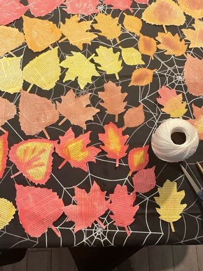 Many leaves cut from book pages watercolored in a variety of shades and combinations. Tucked among them is a spool of white twine.