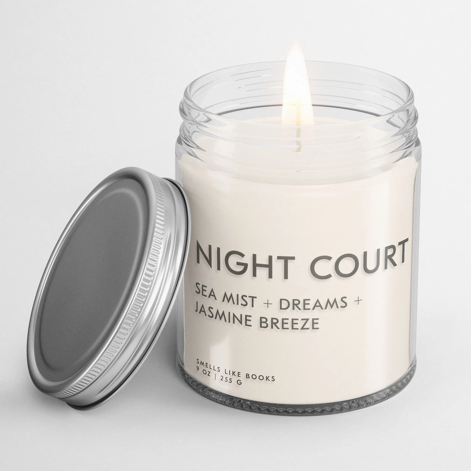 A photo of a white jar candle with a silver top that reads night court sea mist plus dreams plus jasmine breeze in gray lettering. The candle is staged on a white background.