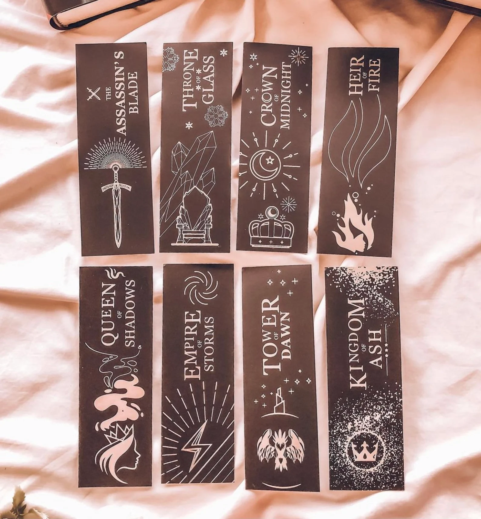 A photo of 8 black bookmarks. Top to bottom, left to right, the bookmarks read The Assasin’s Blade, Throne of Glass, Crown of Midnight, Heir of Fire, Queen of Shadows, Empire of Storms, Tower of Dawn, and Kingdom of Ash.