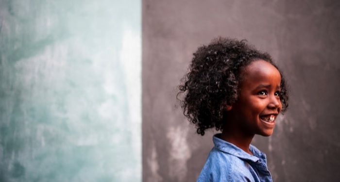 a smiling Black girl with curly brown hair as seen from the side