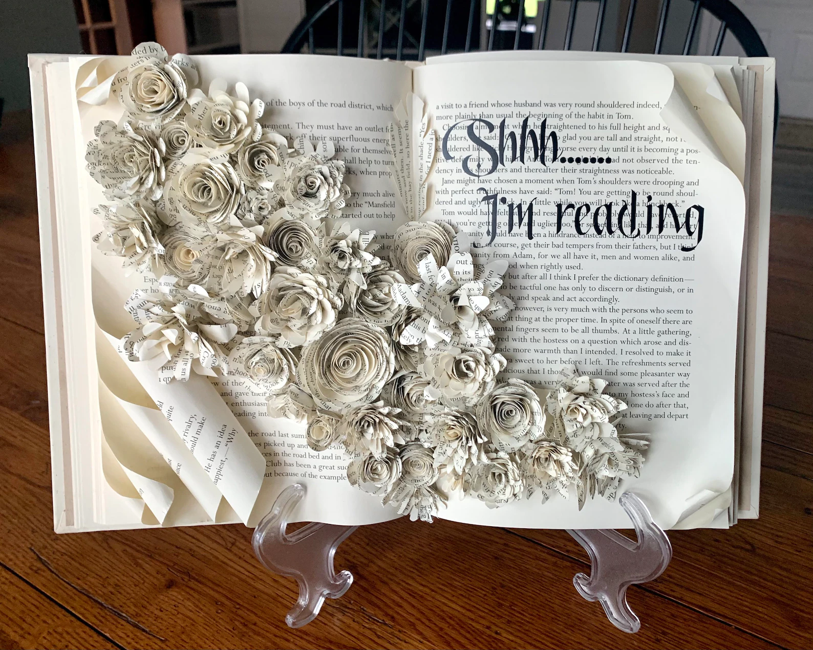 An old book opened to a sculpture of florals made of old pages.