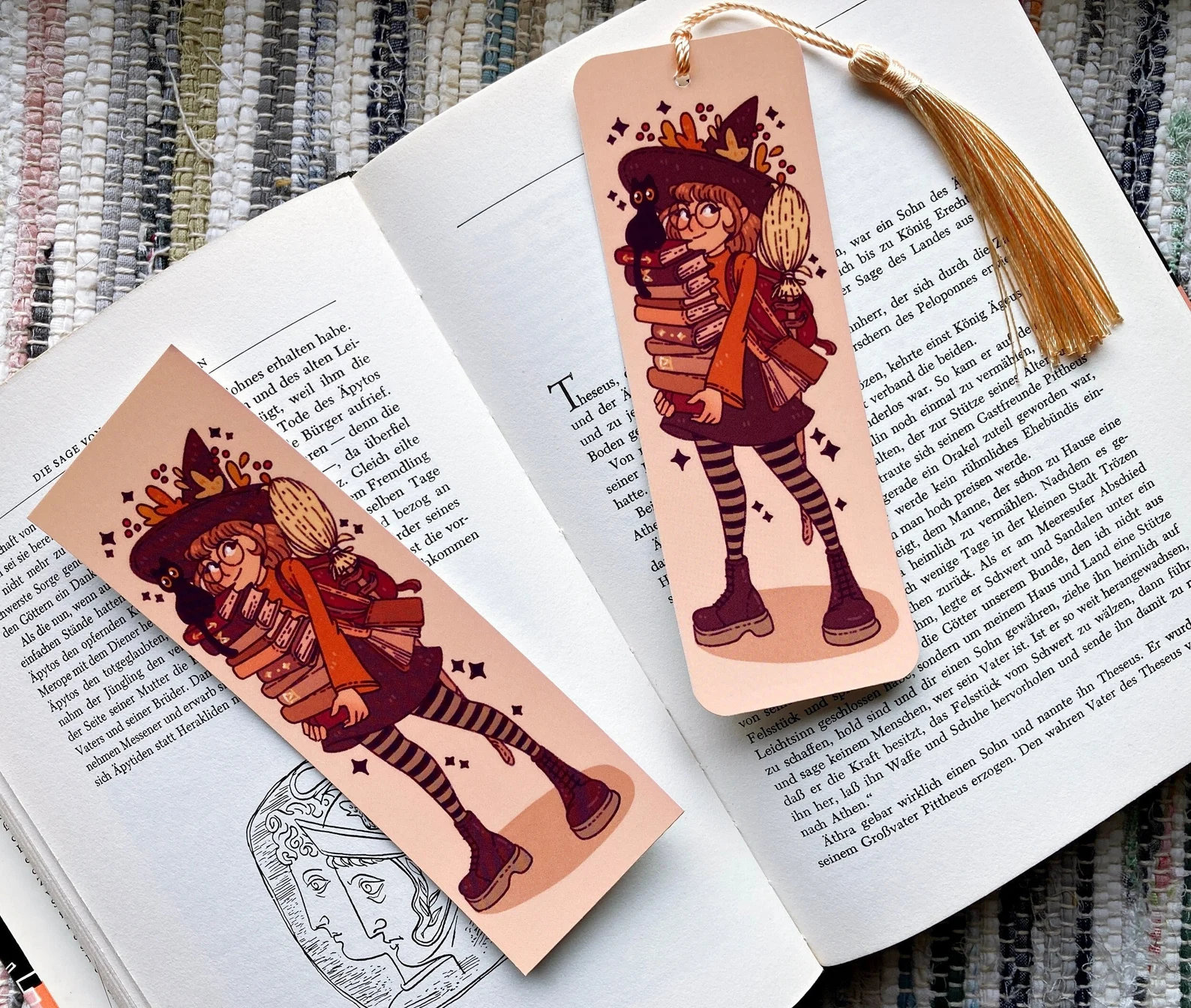 a bookmark placed on an open book featuring a cute witch holding a stack of books