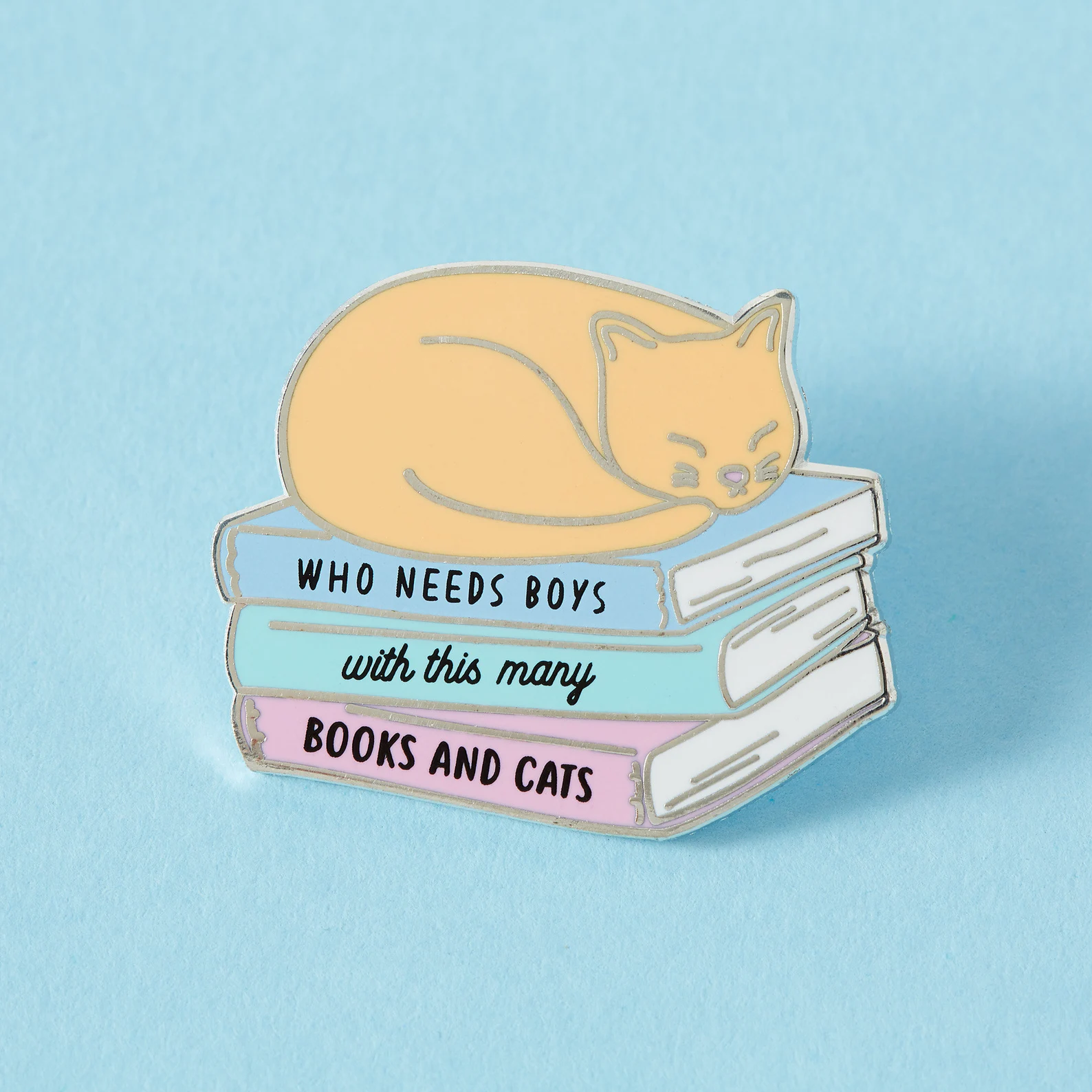 an enamel pin of a cat sleeping on a stack of books that reads "Who needs boys when you have books and cats?"