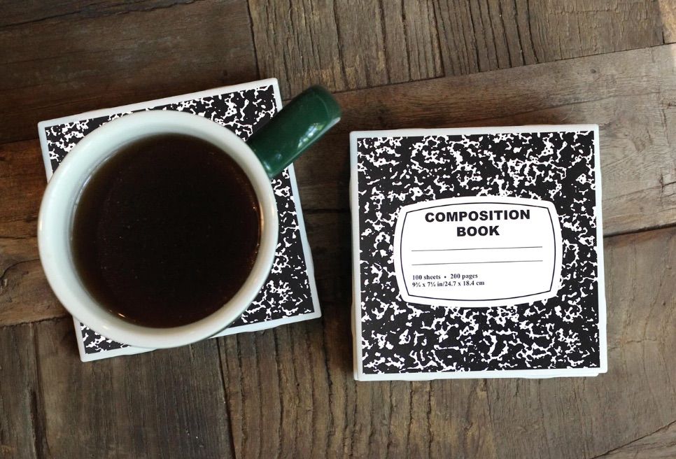 Image of a coaster that looks like a black and white composition book. Beside it, on another coaster, is a coffee cup. 
