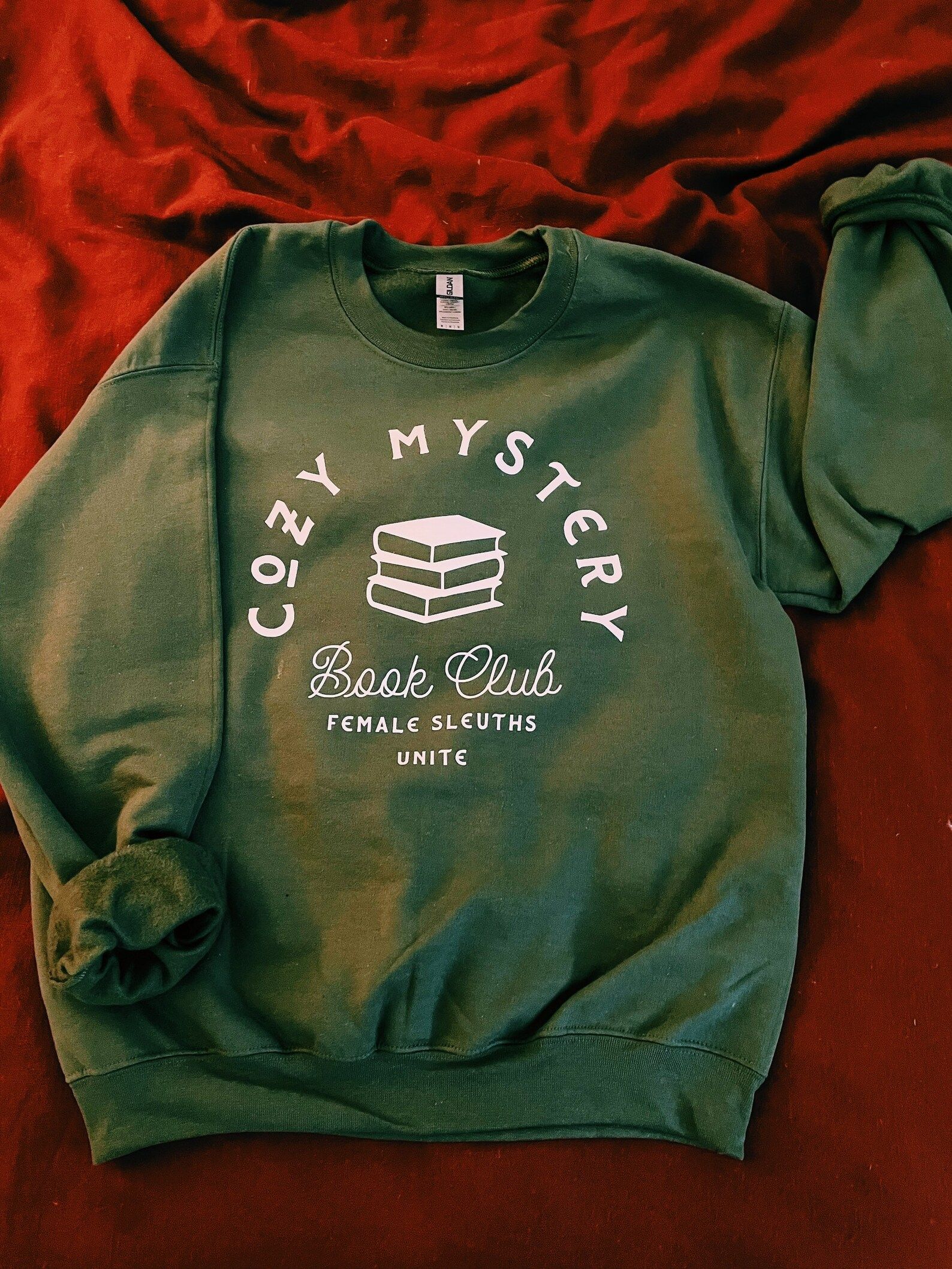Green sweatshirt that reads :cozy mystery book club" with a stack of books and the tagline "female sleuths unite"