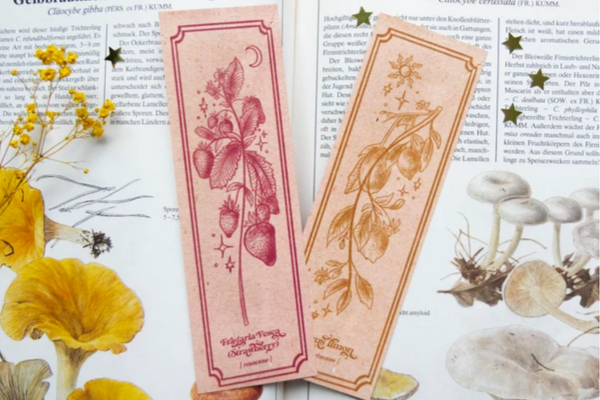 Pink and yellow tinted bookmarks with botanical illustrations of strawberries on one and lemons on the other.