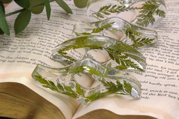 Clear resin thumb book page holders with dried greenery inside laid out artfully along an open book spine