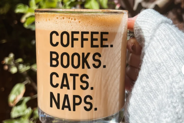 Clear glass coffee mug with black text that reads "Coffee. Books. Cats. Naps."