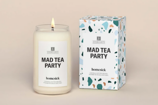 A white candle in a clear glass jar with a white label that reads "Mad Tea Party" in bold black text.