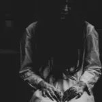 a photo of a woman with long black hair and her face in shadow. Her fingers are dripping with some dark liquid