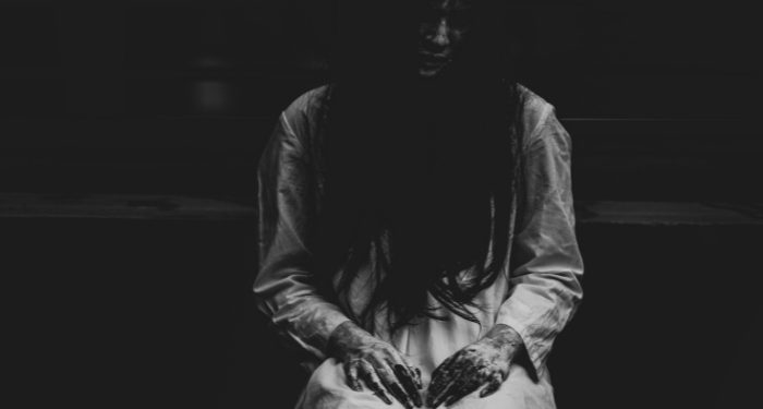 a photo of a woman with long black hair and her face in shadow. Her fingers are dripping with some dark liquid