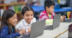 three elementary school-aged children working on laptop computers in a classroom or library