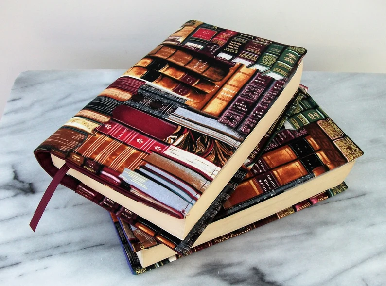 Photo of two stacked books wearing their book sleeves, which have a print of the spine of leather-bound books. 