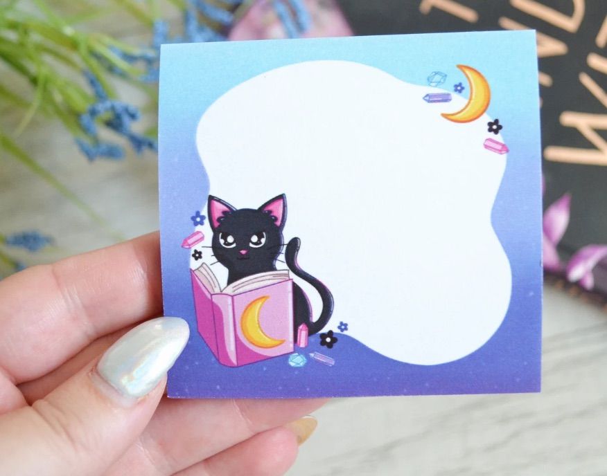 Image of a sticky note set featuring a black cat reading, alongside several crystals. 