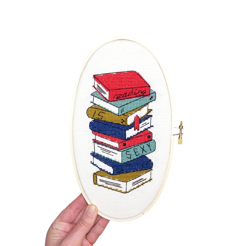 An oval cross stitch with a stack of books that reads "reading is sexy"