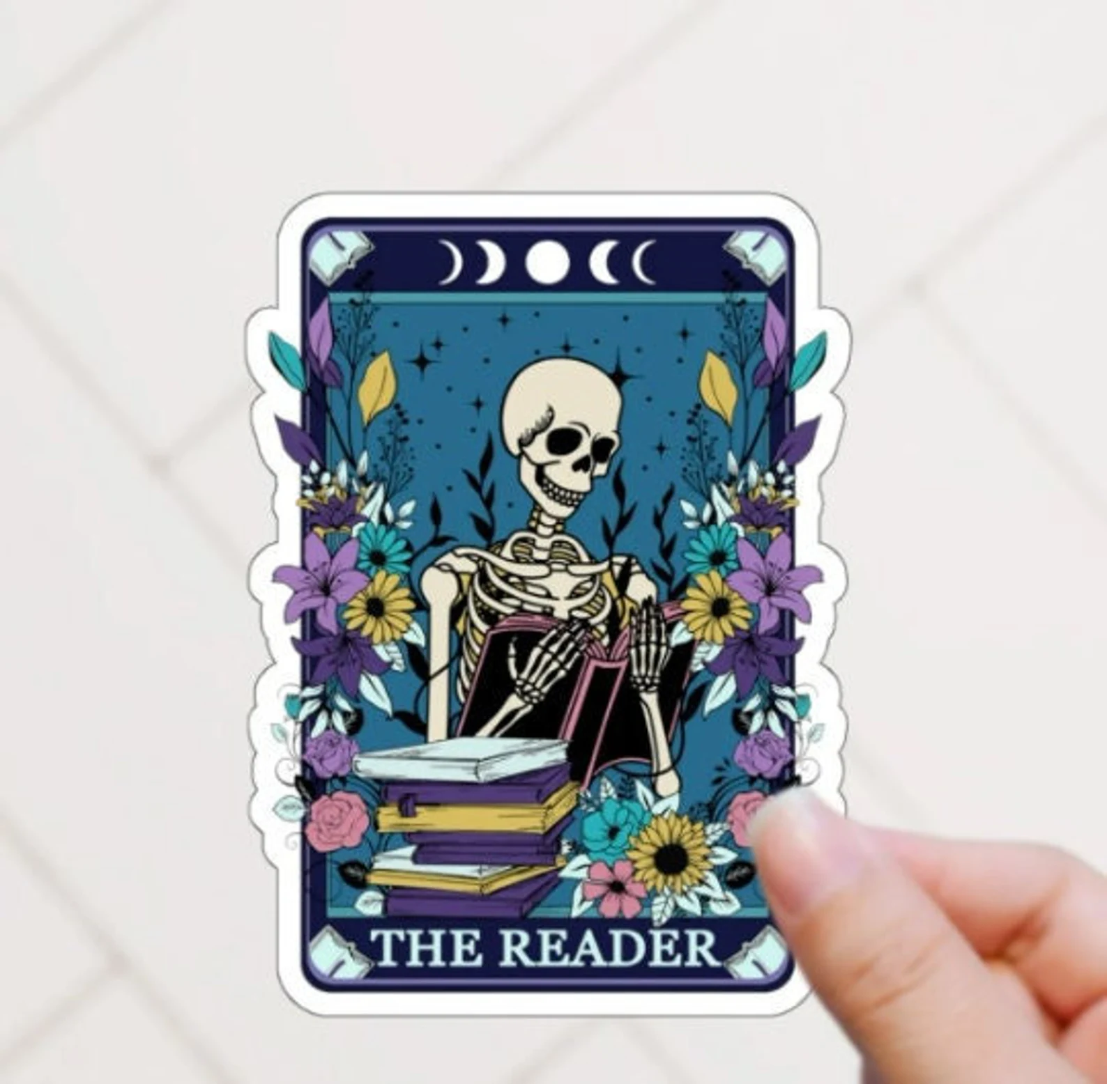 a sticker in the design of a tarot card with a skeleton holding a book