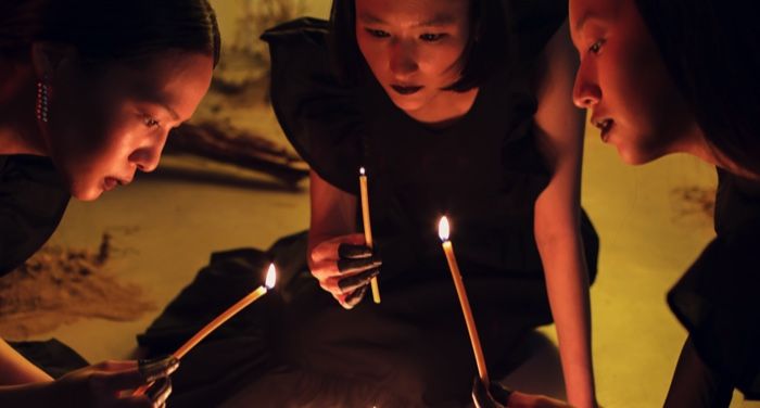 three female Asian witches in a circle with candles in their hands