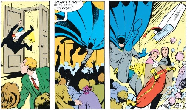 Batman rushes over a crowd and high-kicks a book-bomb away from the British royal family.