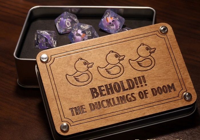 Image of set of resin dnd dice in metal tin with wooden lid saying "Behold!!! The Ducklings of Doom" Transparent dice with light purple duck inside