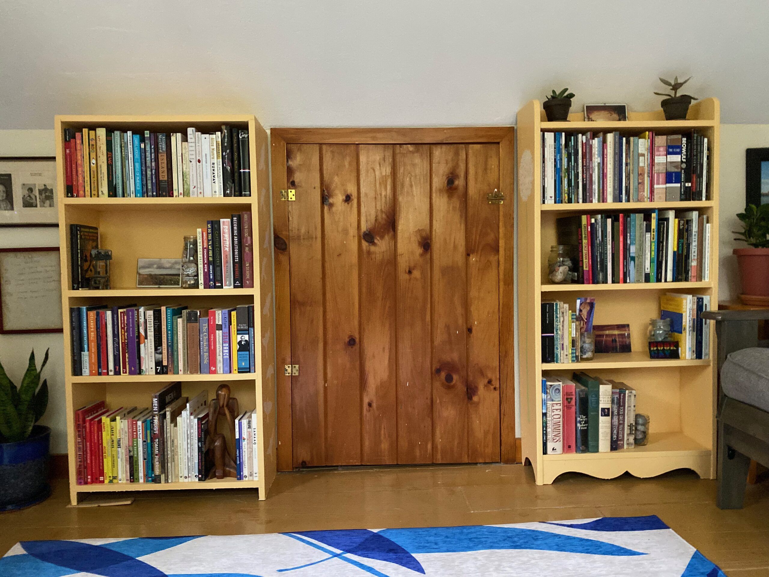 Two yellow bookshelves, full of books, plants, and small knickknacks, on either side of a wooden closet door.