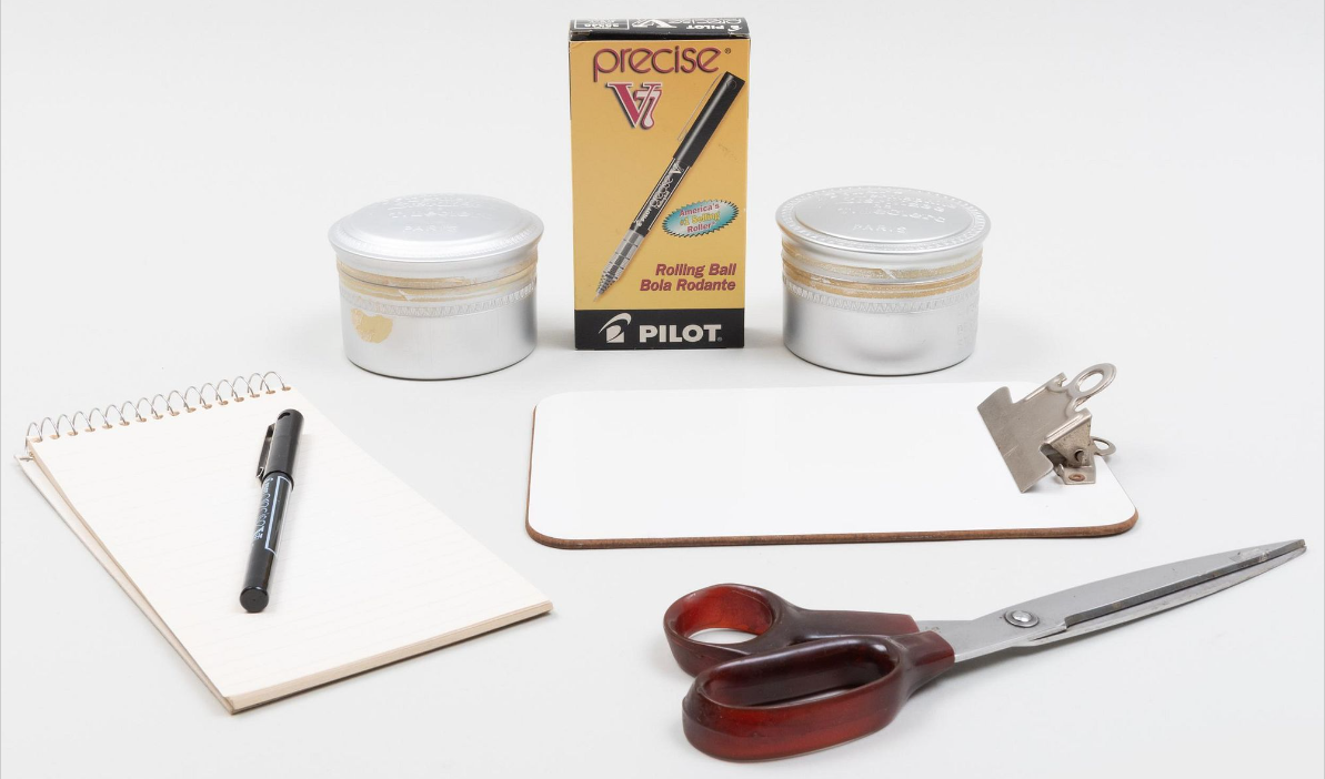 a photo of a blank notebooks, scissors, a box of pens, and containers of pushpins