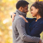 a photo of a Black couple hugging and smiling at a park in the autumn