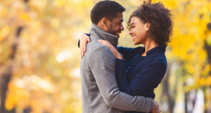 a photo of a Black couple hugging and smiling at a park in the autumn