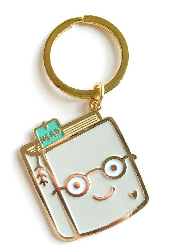 Image of a keychain featuring a book. The book has a face and a bookmark inside that says "read."