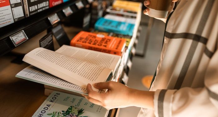 a photo of someone flipping through a book on a bookstore display table while holding a coffee cup