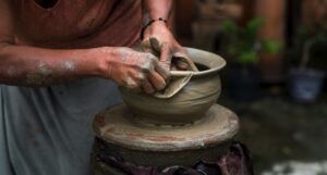 hands molding clay into a pot on a throwing wheel